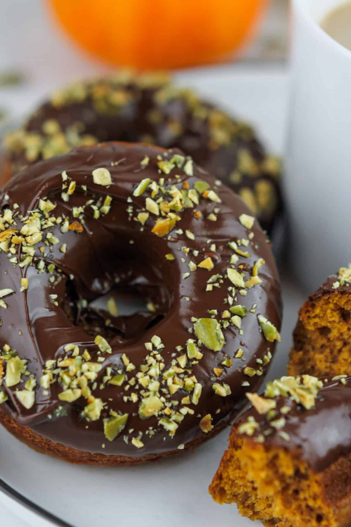 very close-up shot of chocolate dipped pumpkin donuts sprinkled with chopped pumpkin seed sprinkled on top.