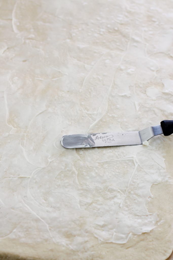 Butter spread on flat unbaked cinnamon roll dough with a metal spatula.