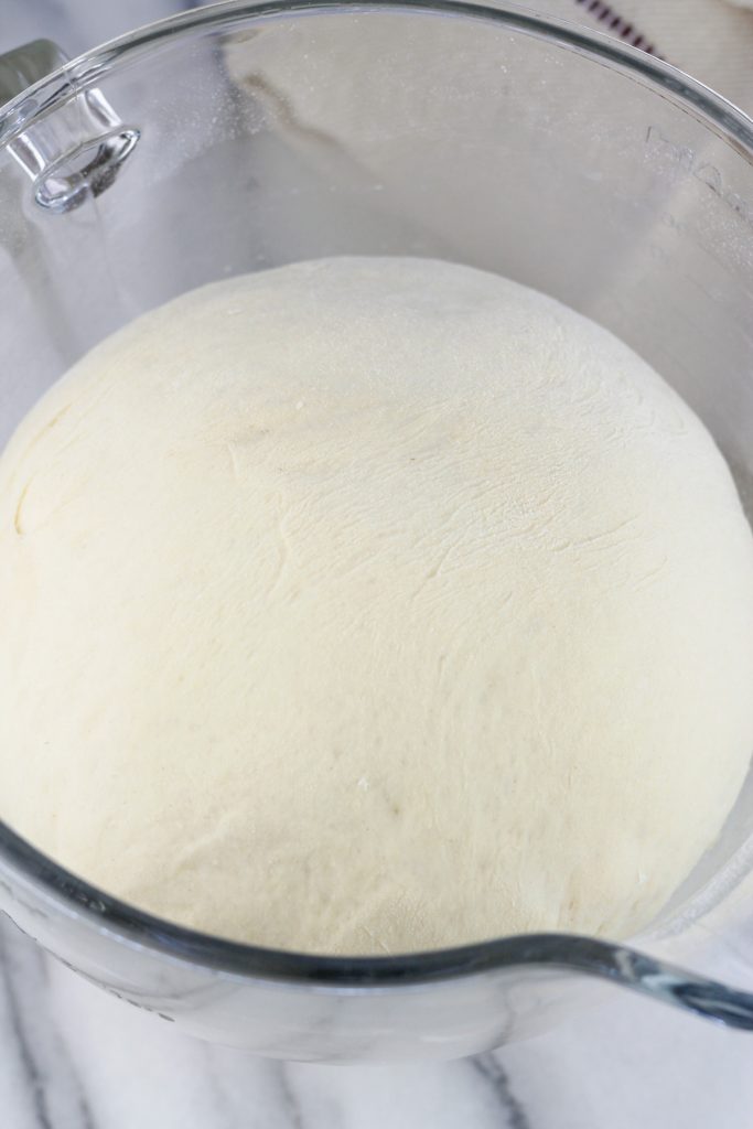 Overhead shot of proofed dough in glass mixing bowl of a Kitchenaid mixer.