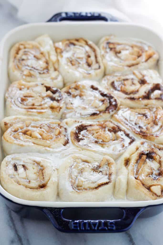 Rolled unbaked cinnamon rolls in a baking dish with heavy cream poured o top.