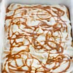 Shot of baked caramel apple cinnamon rolls with cream cheese topping and swirls of caramel on top in a baking dish.