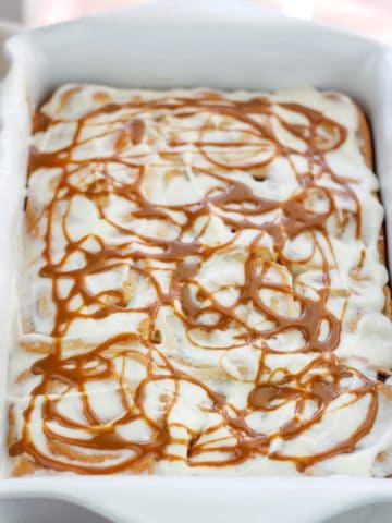 Shot of baked caramel apple cinnamon rolls with cream cheese topping and swirls of caramel on top in a baking dish.