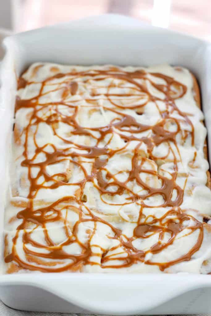 Shot of baked caramel apple cinnamon rolls with cream cheese topping and swirls of caramel on top in a baking dish.