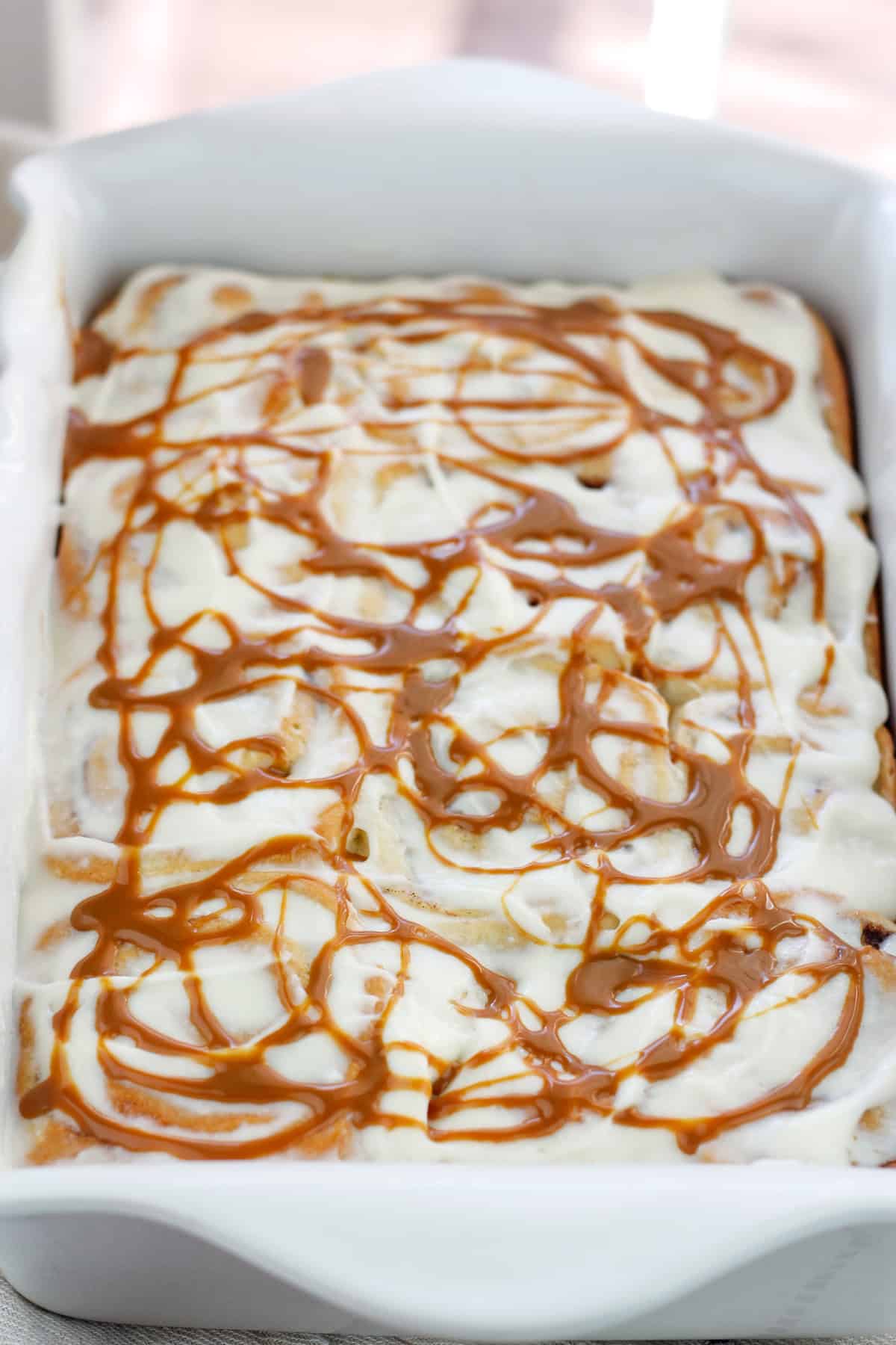 Shot of baked caramel apple cinnamon rolls with cream cheese topping and swirls of caramel on top in a baking dish.