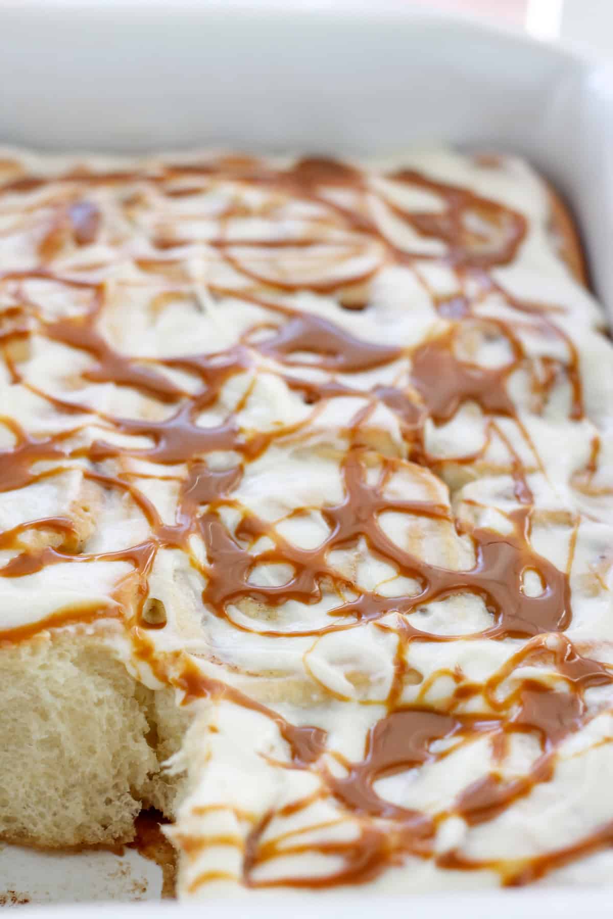 Shot of baked caramel apple cinnamon rolls with cream cheese topping and swirls of caramel on top in a baking dish.