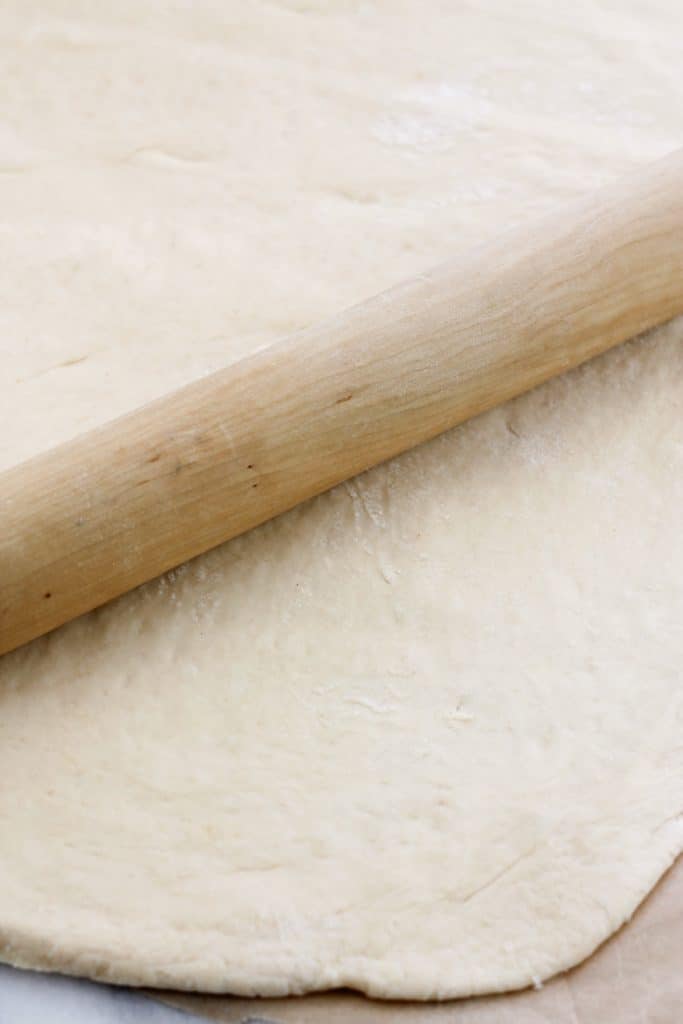 Wooden rolling pin on flat unbaked cinnamon roll dough.