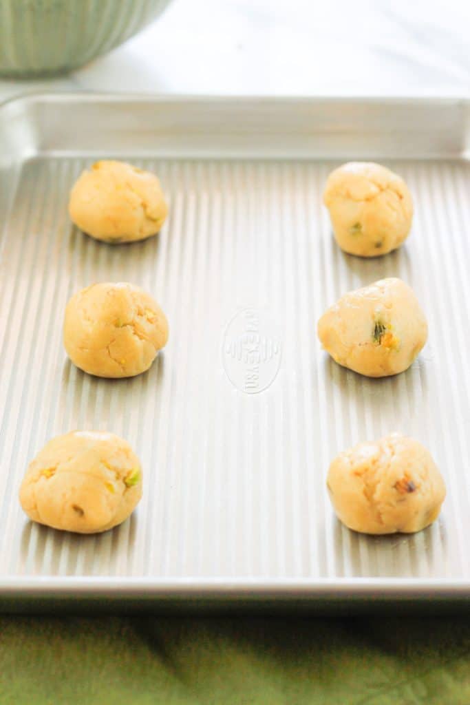 Balls of unbaked pistachio cookie dough on a baking sheet.