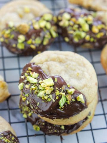 Chocolate Dipped Pistachio Nut cookies on a cooling rack, stacked.