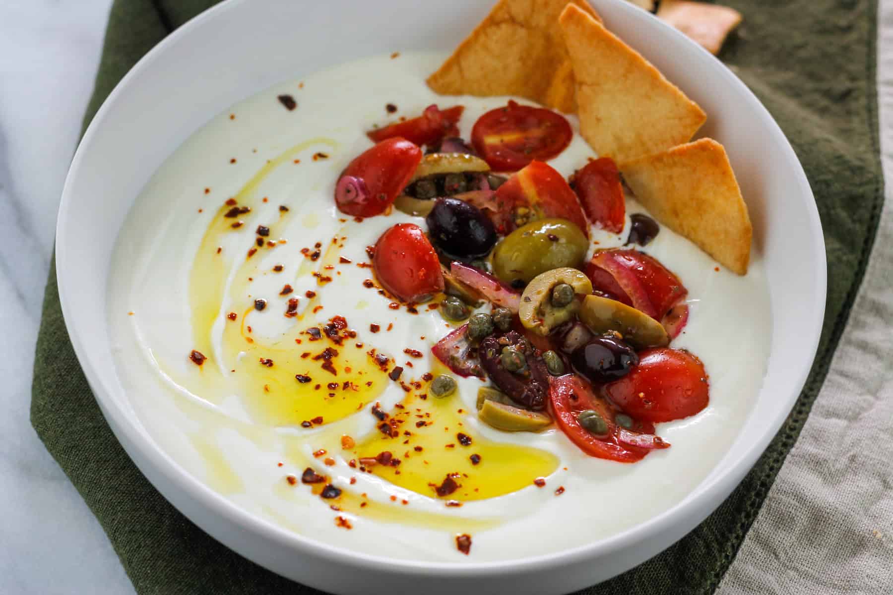 Close-up shot of a bowl filled with whipped feta garnished with olive oil, aleppo pepper flakes and crispy pita chips.