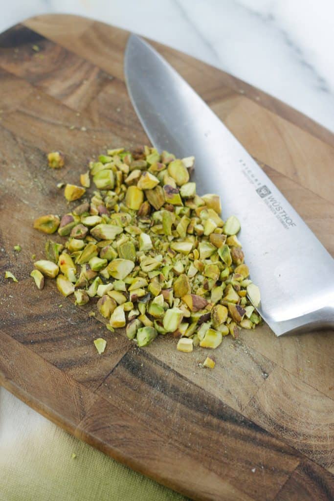 Rough chopped pistachio nuts on a cutting board with knife.