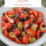 Angle overhead shot of tomato and olive salad in a bowl placed on top of a dark green kitchen towel.