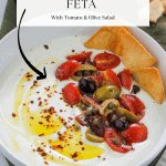 Overhead angled shot of a bowl filled with whipped feta garnished with olive oil, aleppo pepper flakes and some tomato and olive salad with crisp pita chips at the top right side of the bowl.