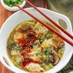 Overhead potsticker soup garnished with sesame seeds and spicy chili onion crunch and red chopsticks.