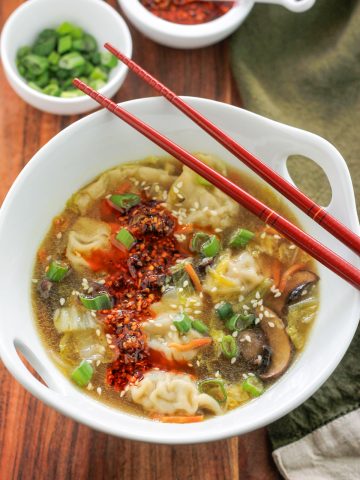 Overhead potsticker soup garnished with sesame seeds and spicy chili onion crunch and red chopsticks.