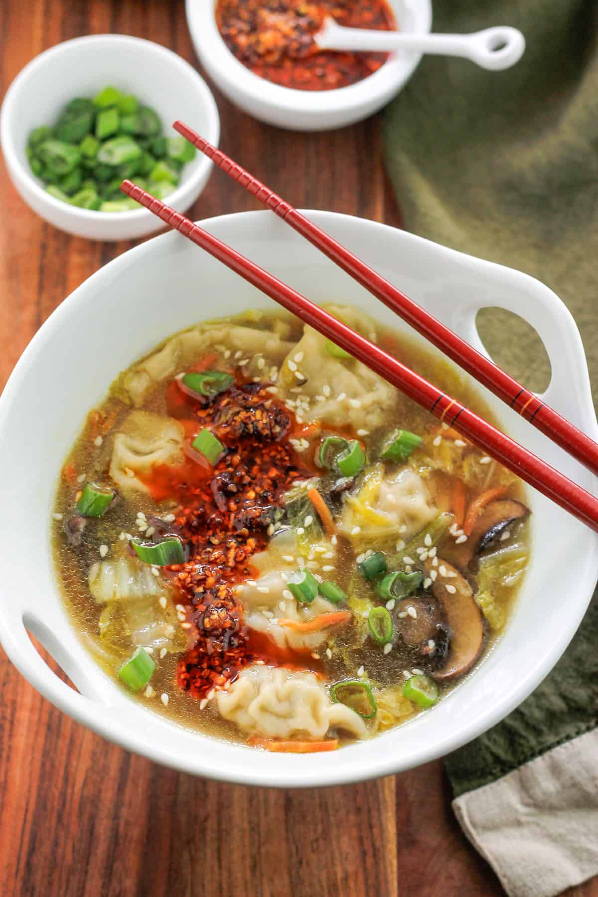 Overhead potsticker soup garnished with sesame seeds and spicy chili onion crunch and red chopsticks.