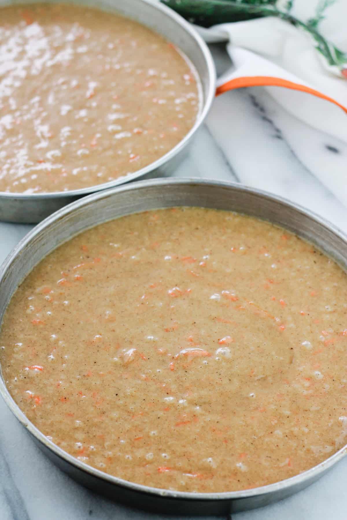 Unbaked carrot cake batter in prepared cake pans.