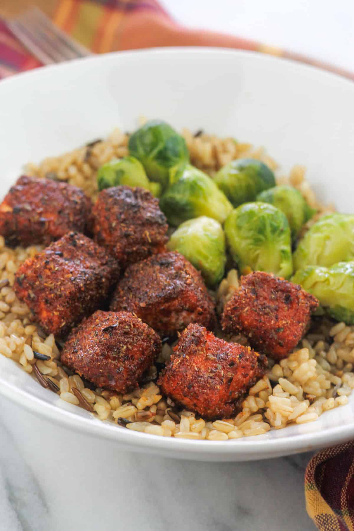 Spicy Air fryer salmon bites and brussel sprouts in a bowl with brown and wild rice.