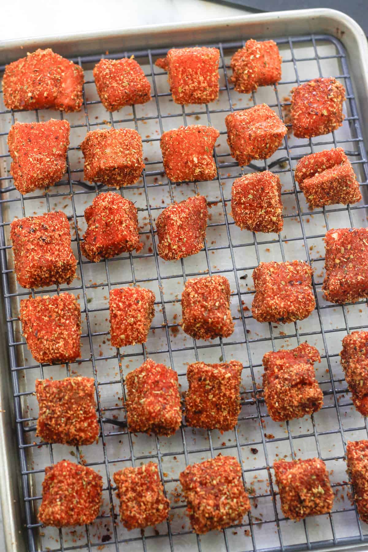 Cubed salmon tossed in spice and herb mixture on baking rack.