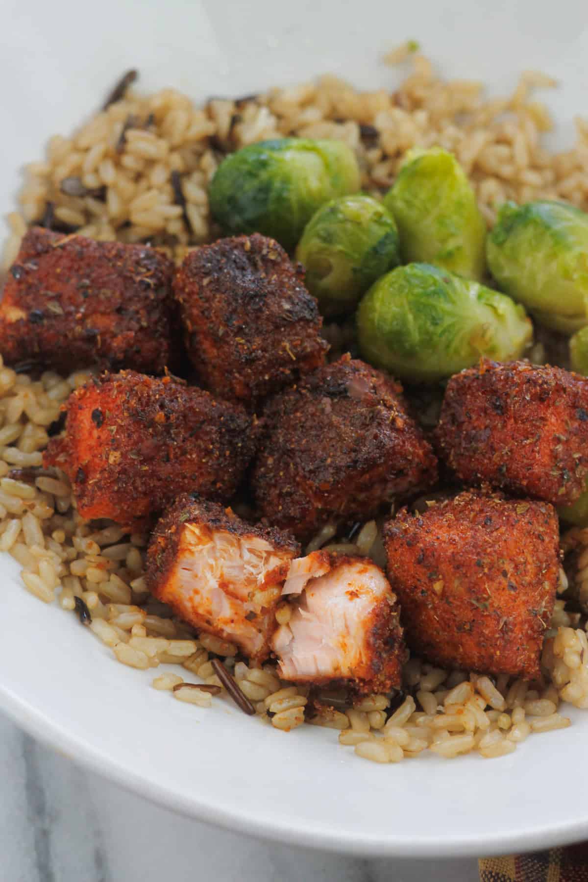 Spicy Air fryer salmon bites and brussel sprouts in a bowl with brown and wild rice.