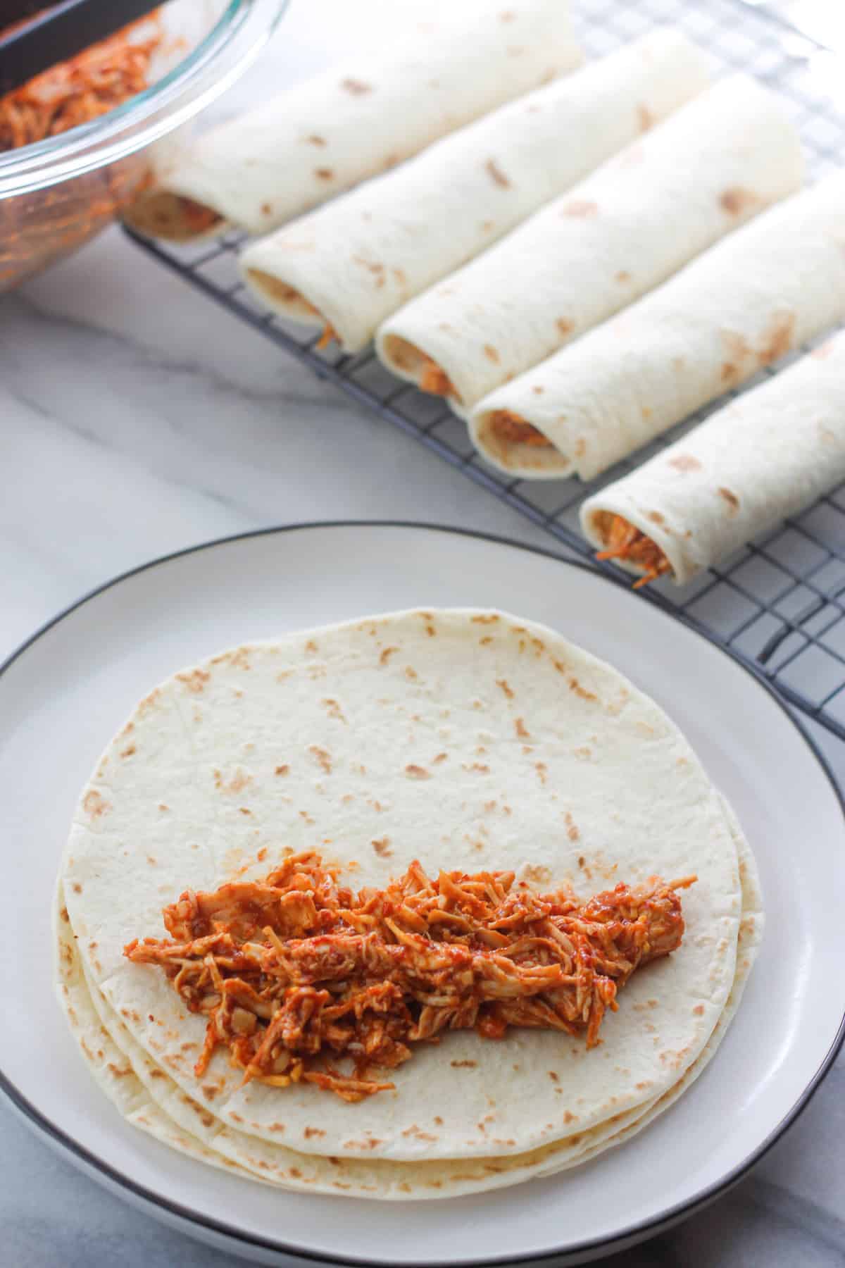 Chipotle chicken filling on a flour tortilla with rolled taquitos at the back right.