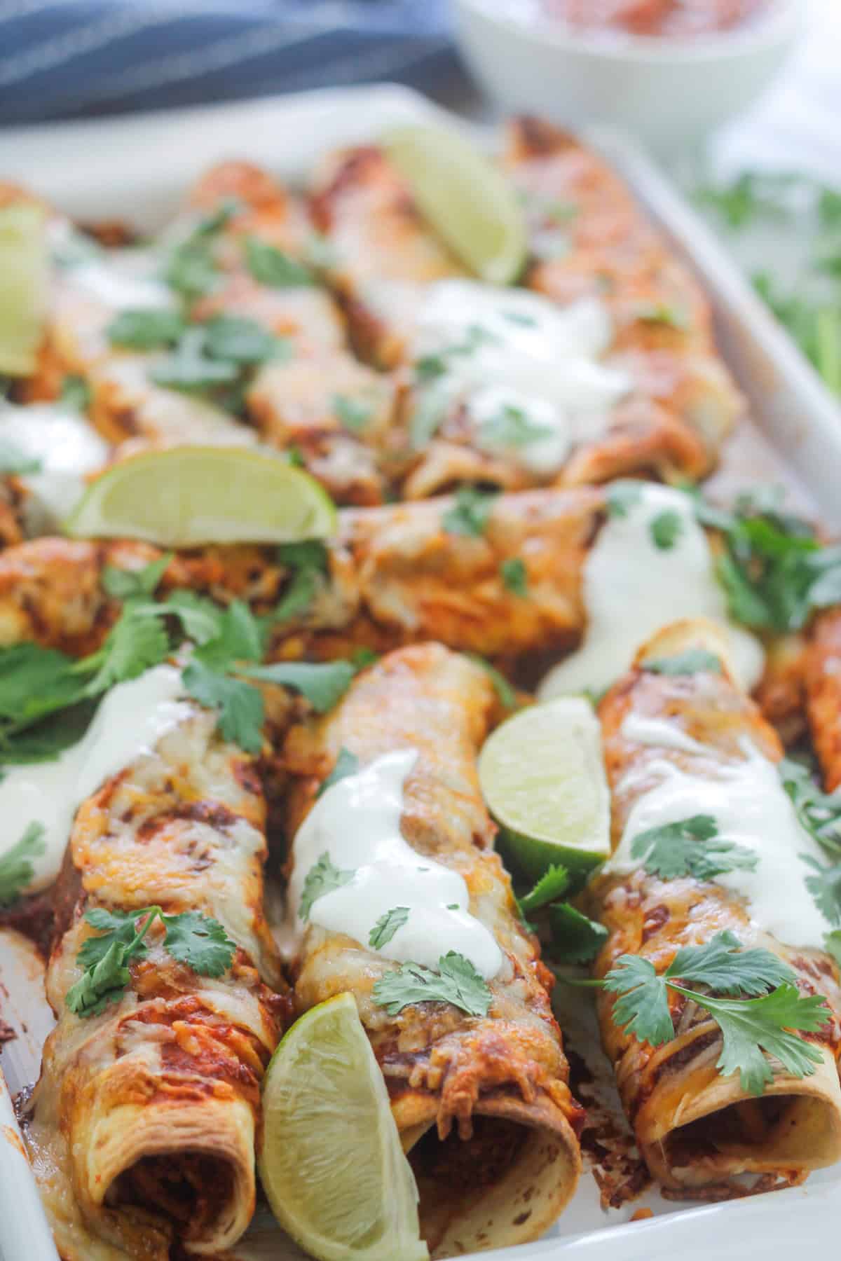 Close shot of a platter of baked chipotle chicken taquitos garnished with sour cream and cilantro.