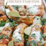 Platter of baked chipotle chicken taquitos garnished with sour cream, cilantro, and lime wedges.