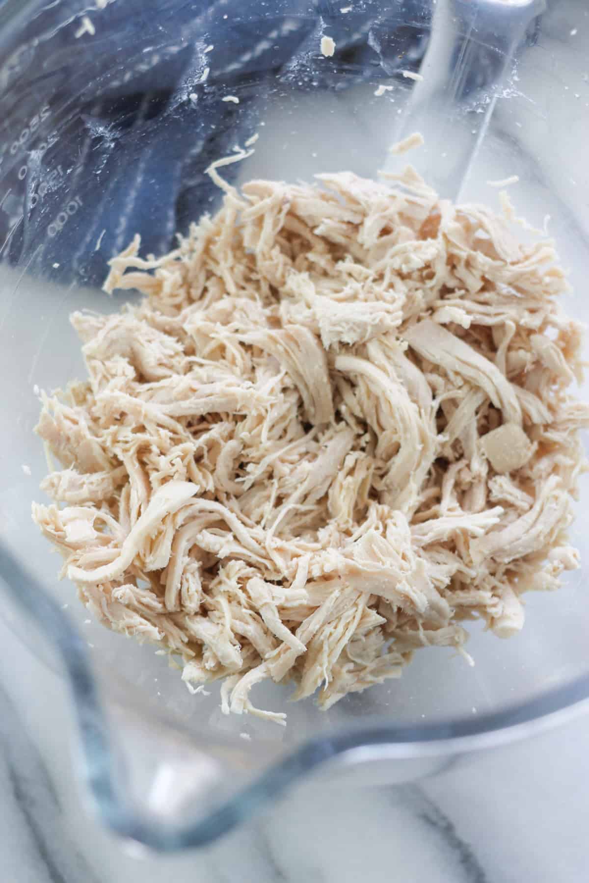 Shredded chicken in the bowl of a kitchenaid stand glass mixer bowl.