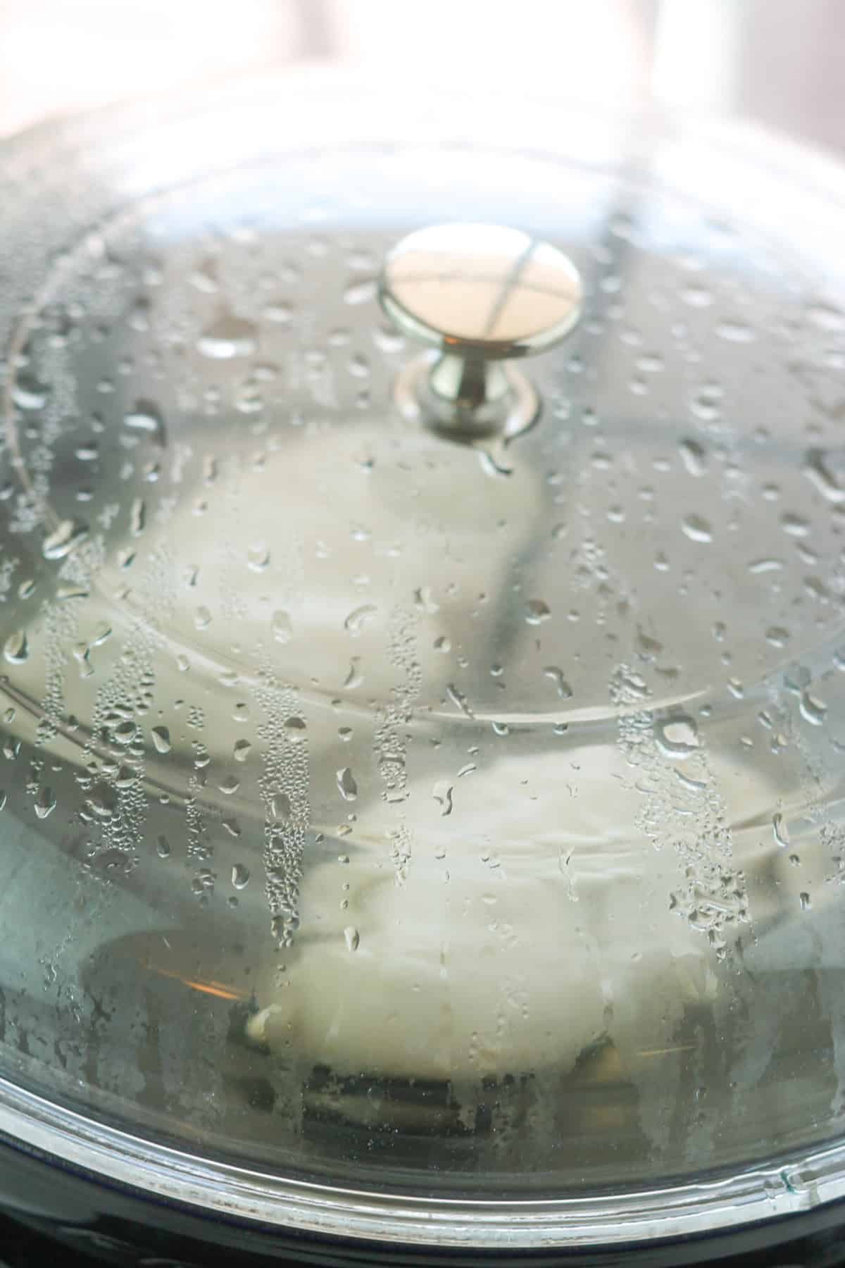 Two chicken breast simmering in pan with lid on the pan.