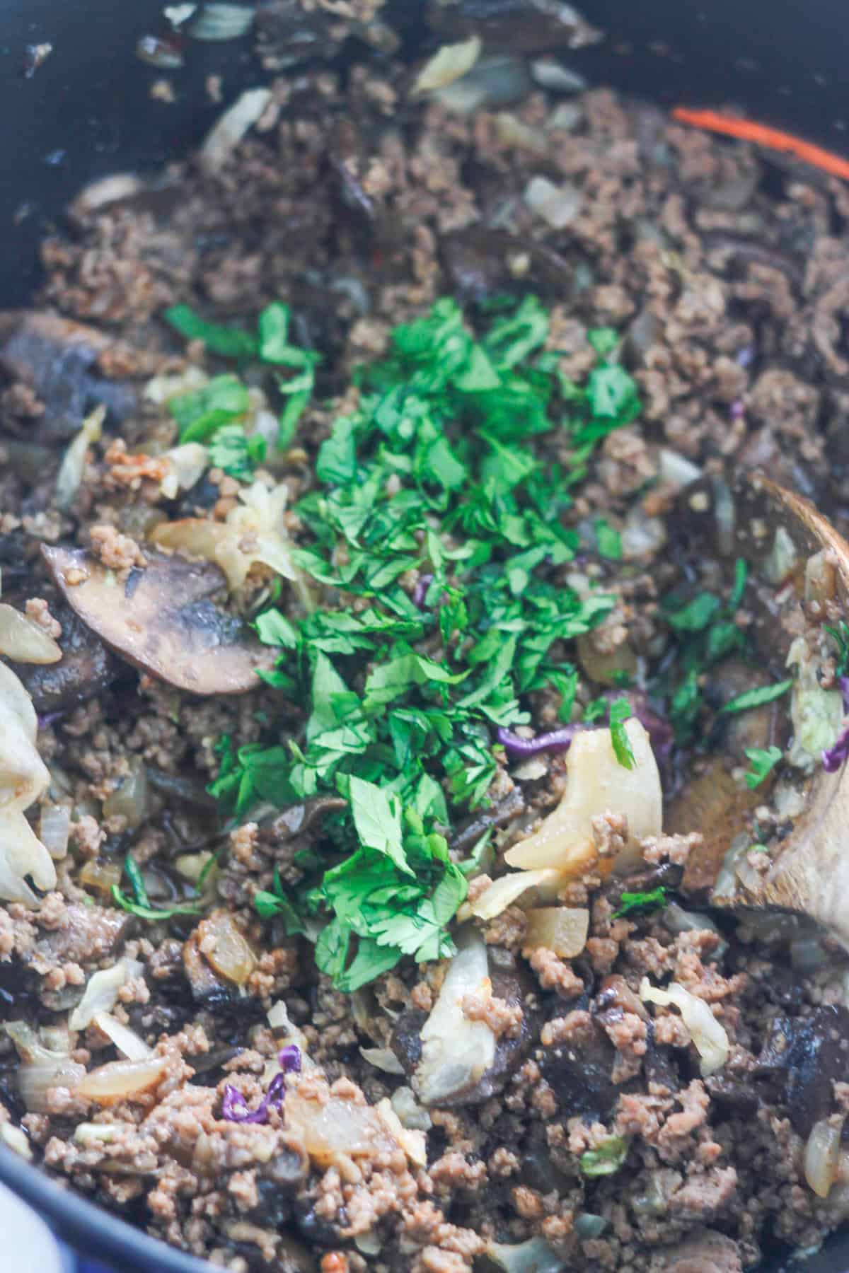 Chopped cilantro added to seasoned ground meat mixture.