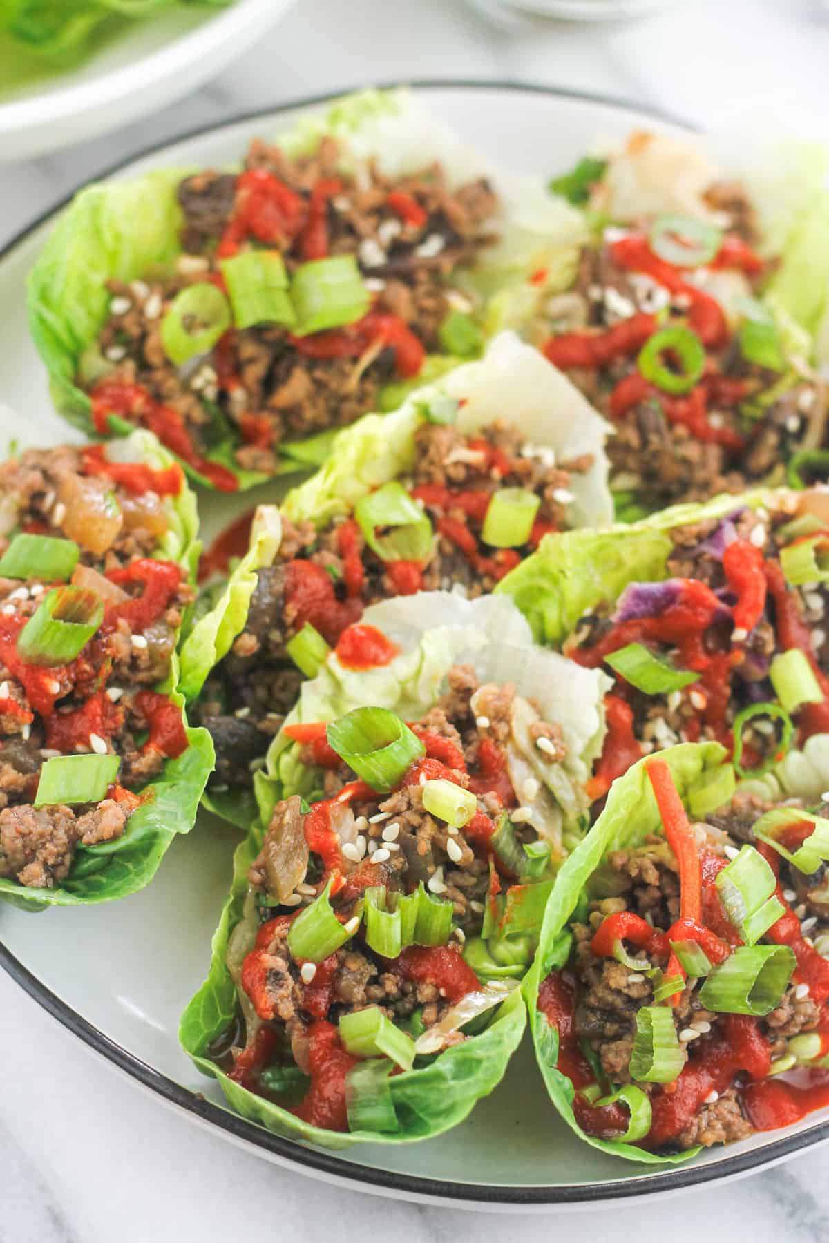 Platter of Low-Carb Asian-Style Ground Meat Lettuce Wraps garnished with sliced green onions, toasted sesame seeds and sriracha.
