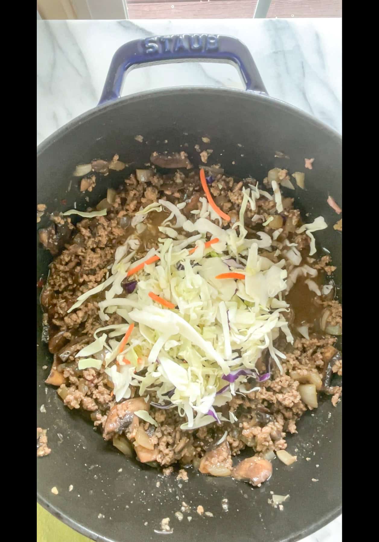 Seasoned ground meat in pan with coleslaw mix on top.