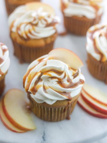 Apple cider cupcakes with cream cheese frosting garnished with caramel sauce and apple slice.
