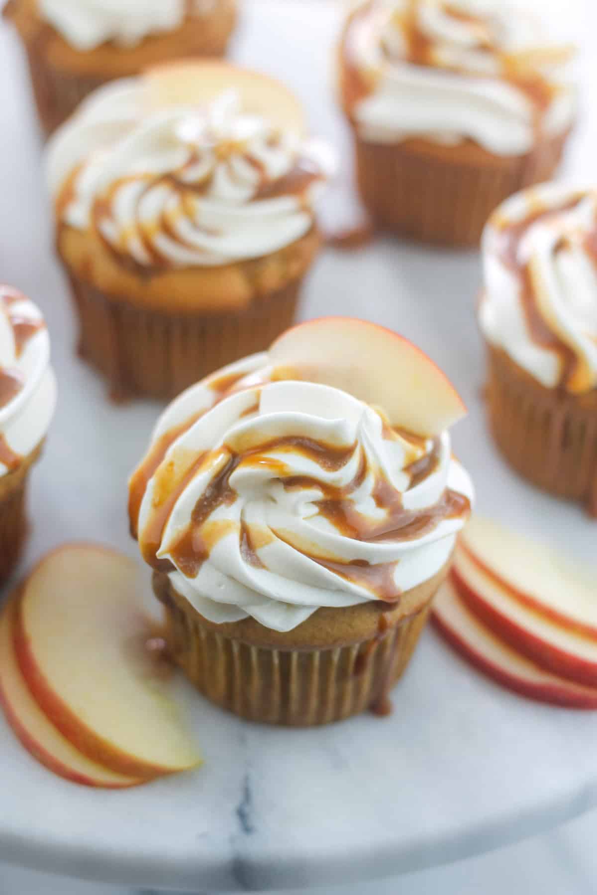 Apple cider cupcakes with cream cheese frosting garnished with caramel sauce and apple slice.