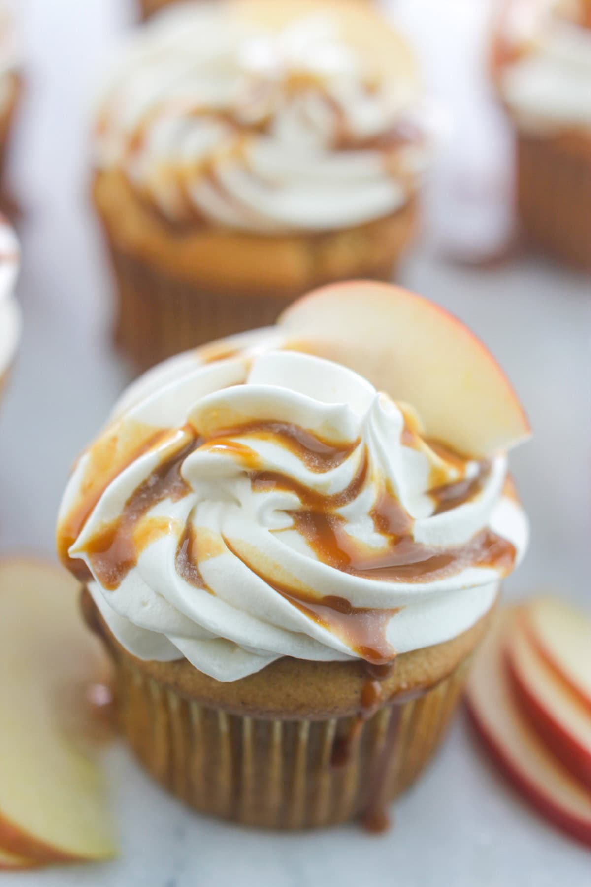 Close-up of apple cider cupcakes with cream cheese frosting garnished with caramel sauce and apple slice.