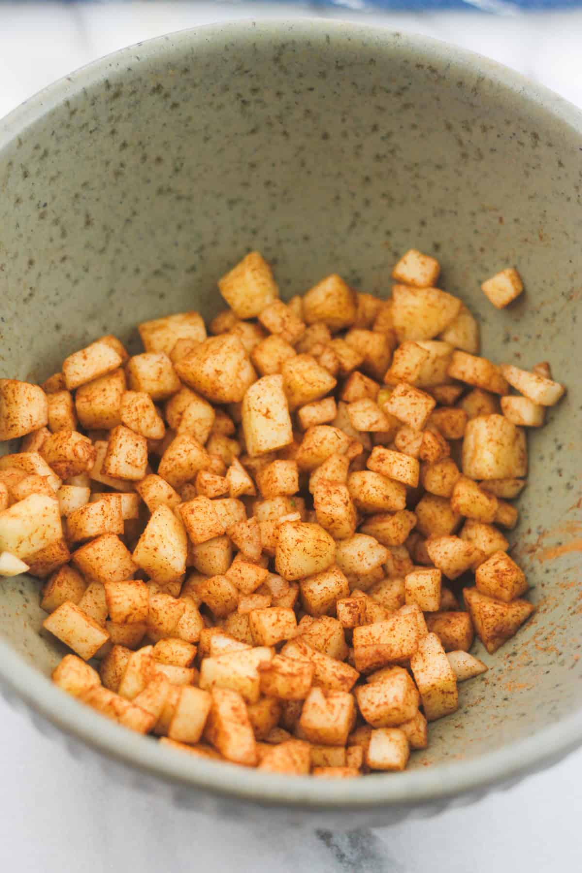 Diced apples in bowl tossed with ground cinnamon.