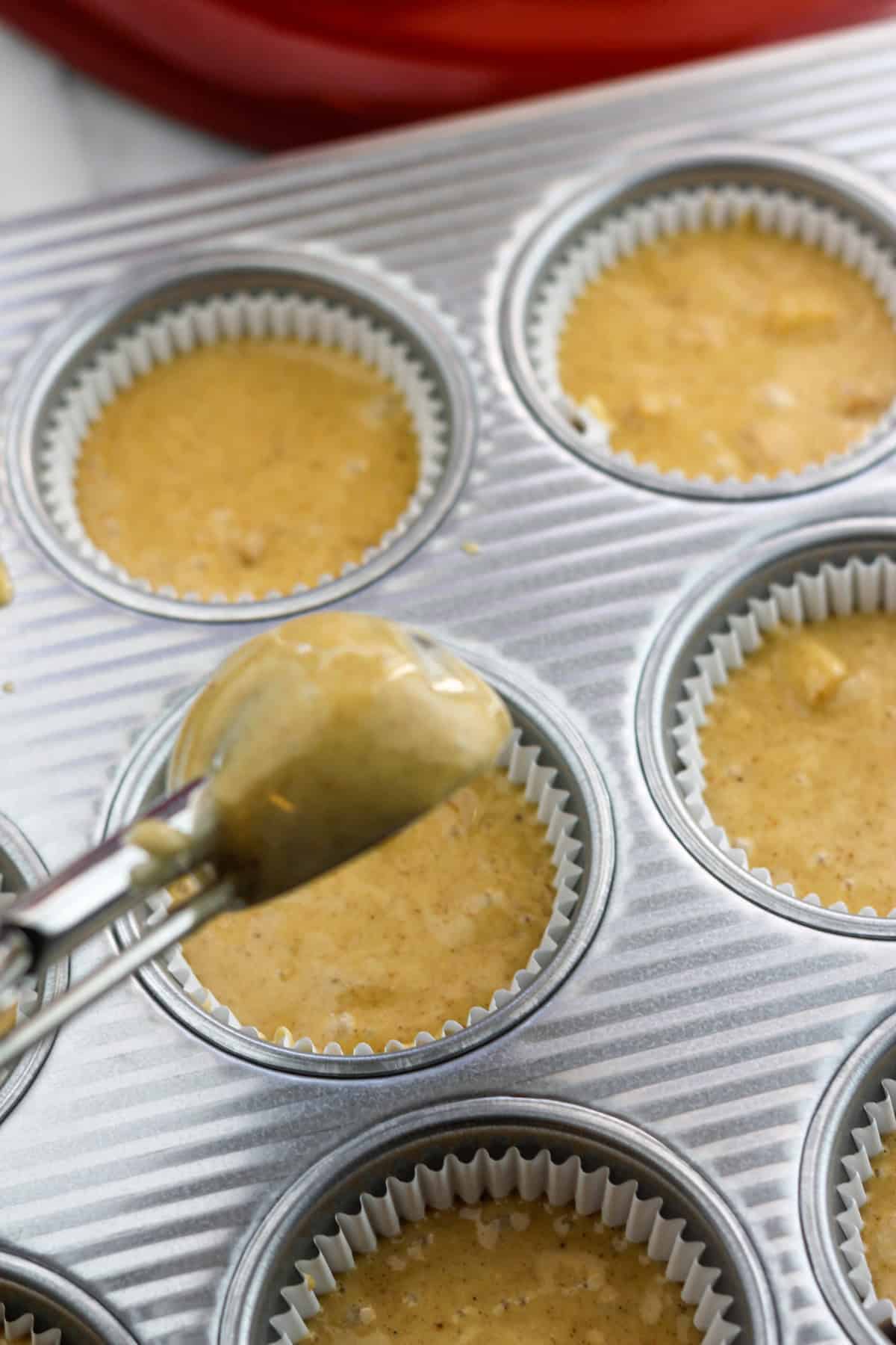 Paper lined muffin pan being filled with cake batter using an ice cream scoop.