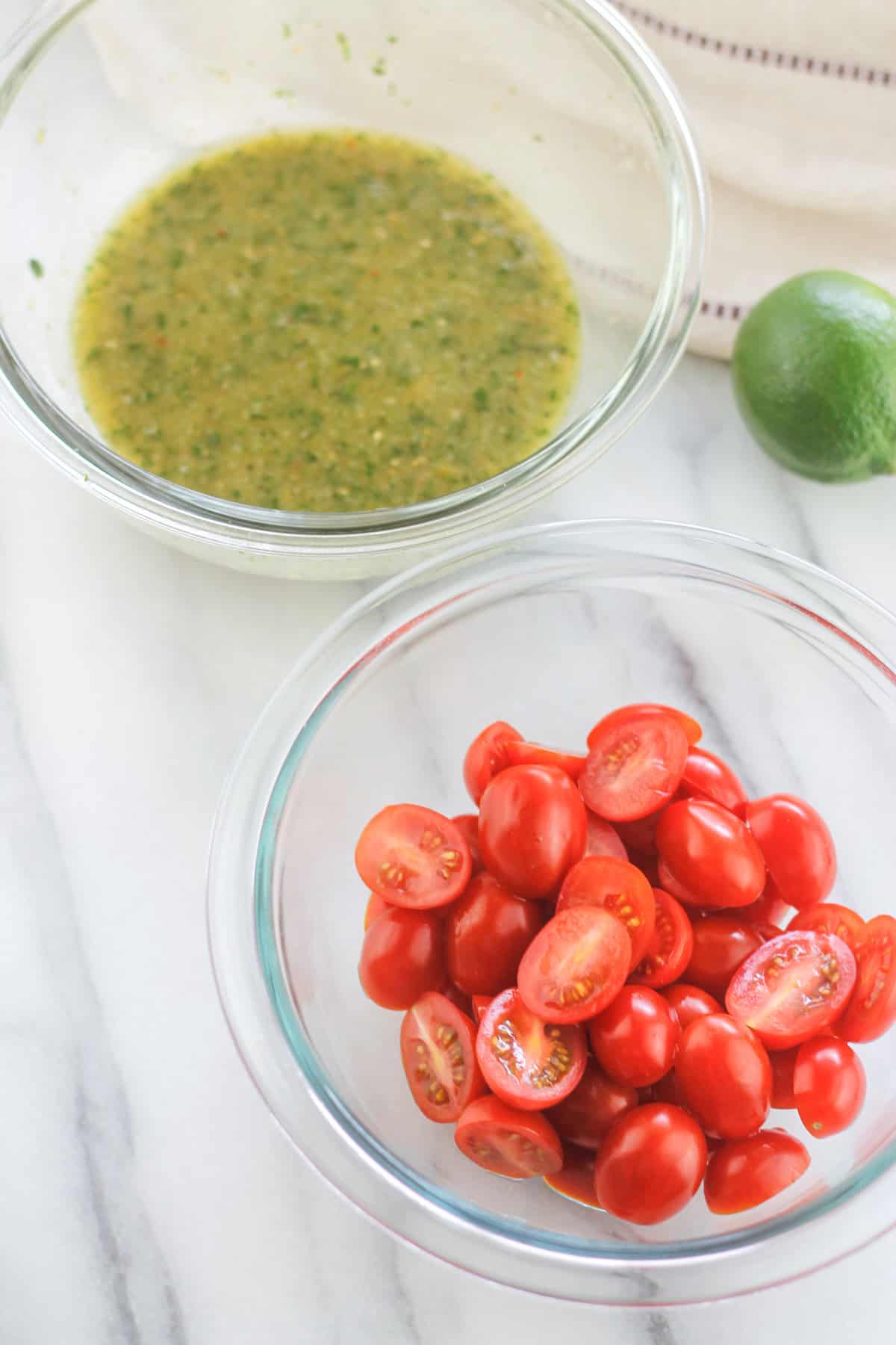 Sliced cherry tomatoes in a glass bowl and cilantro sauce in a glass bowl.