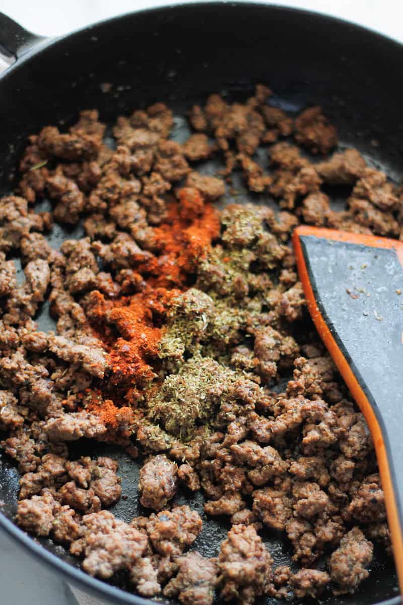 Ground beef cooking in a skillet with Italian seasoning and paprika.