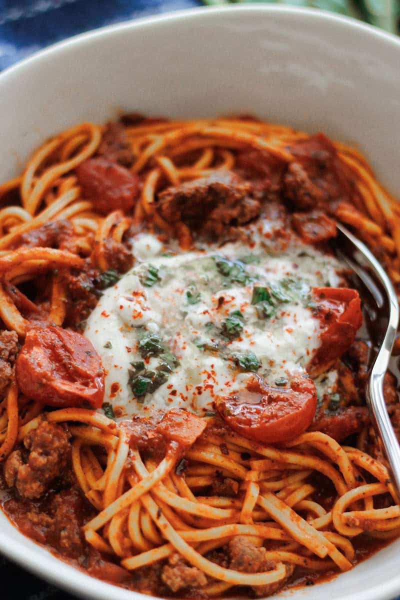Close-up shot of a bowl full of Beefy spaghetti pasta with burrata and lemon basil oil.