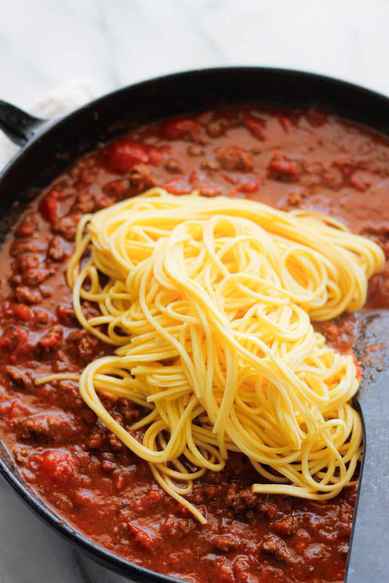 Cooked spaghetti pasta added to meat sauce.