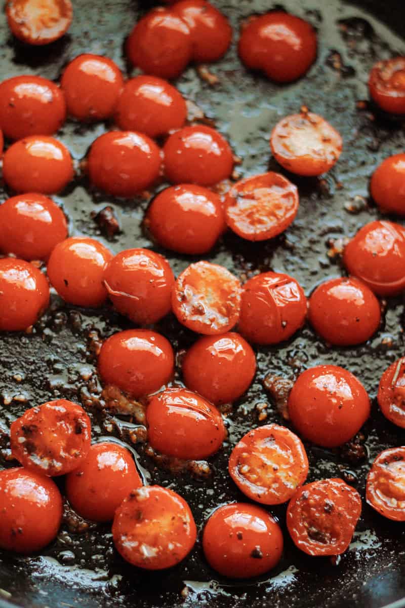 Halved cherry tomatoes and garlic cooking in a skillet.