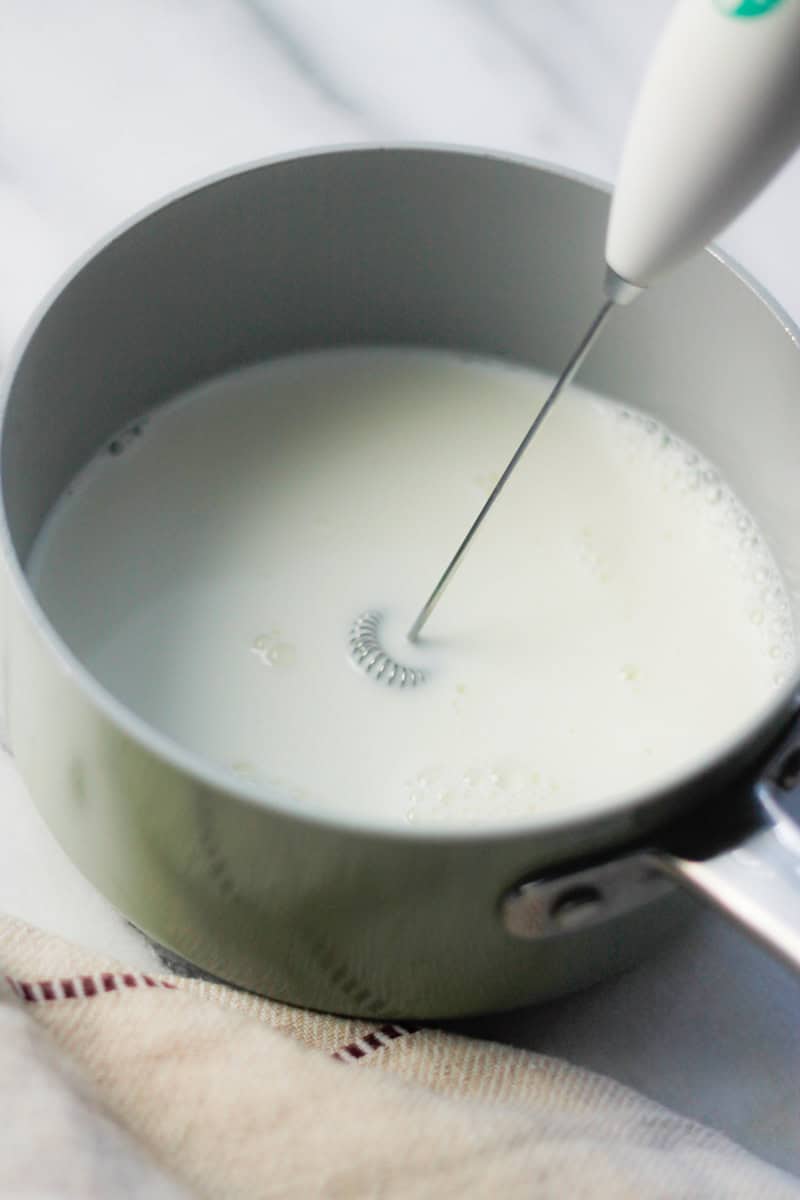 Handheld frother frothing milk in a saucepan.