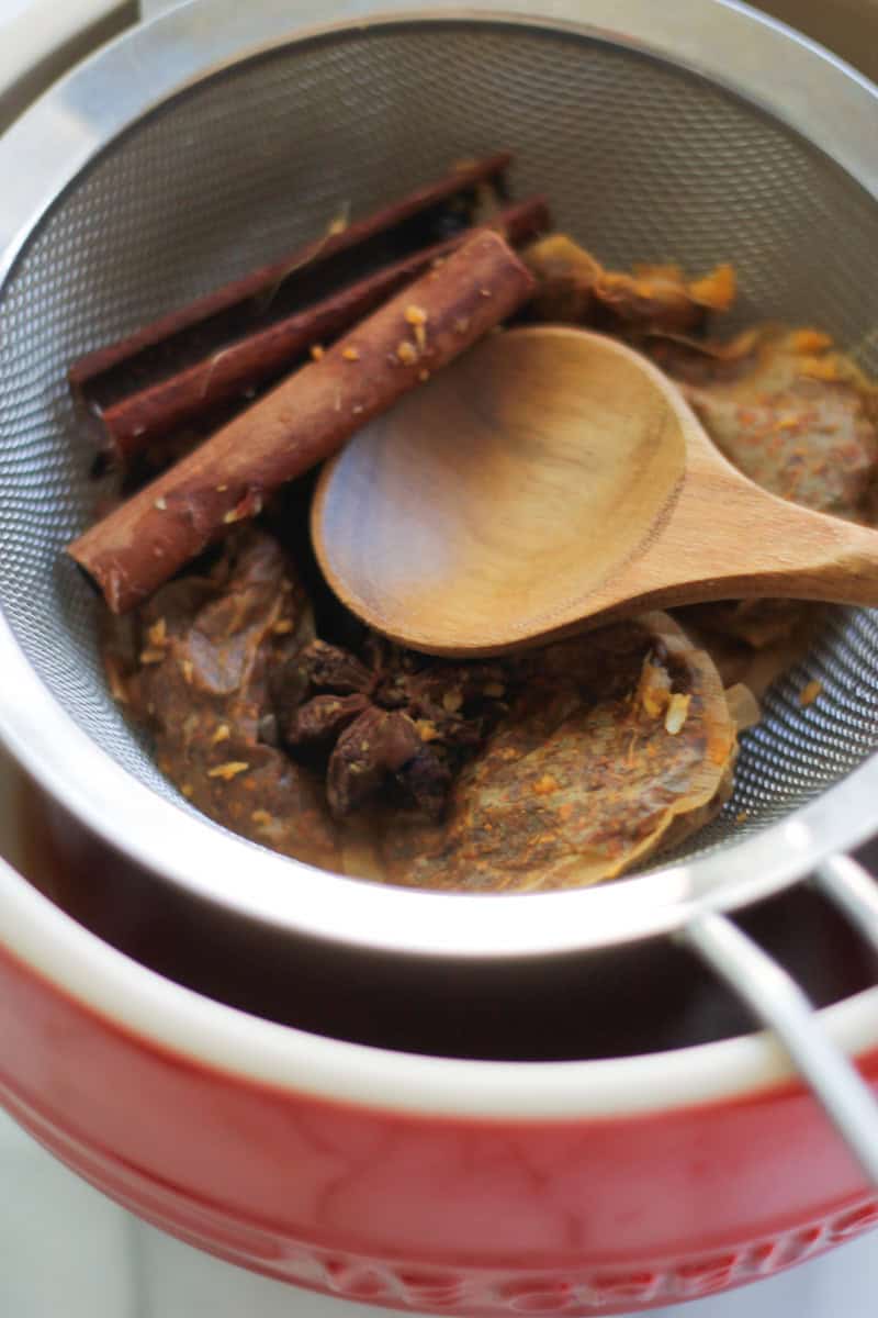 Spices and rooibos tea bags in a fine mesh strainer over a bowl.