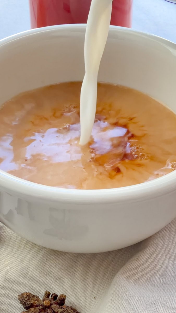 Steamed milk pouring into Rooibos Chai Tea in a white mug.